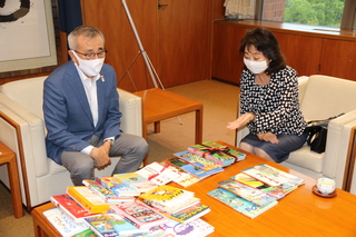 相良代表取締役から本の説明を受ける奥塚市長（写真左）