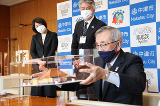 いただいたペーパークラフトの福澤諭吉旧居を手に取る奥塚市長（写真前列）