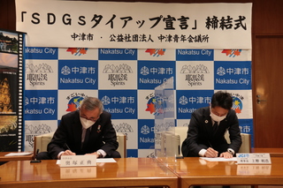 タイアップ宣言に署名する奥塚市長（写真左）
