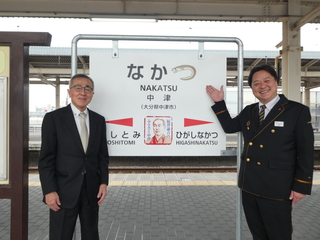 駅の看板と中津市長（写真左）